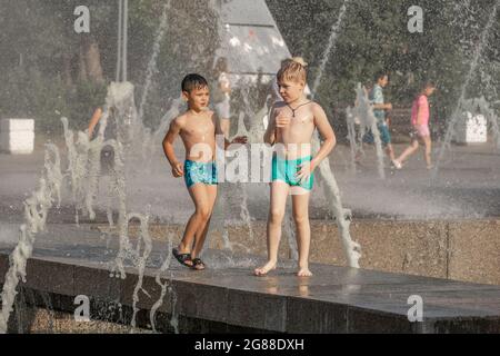Two boys playing in jets of water fountain, seen through sprays and droplets, in Summer Stock Photo