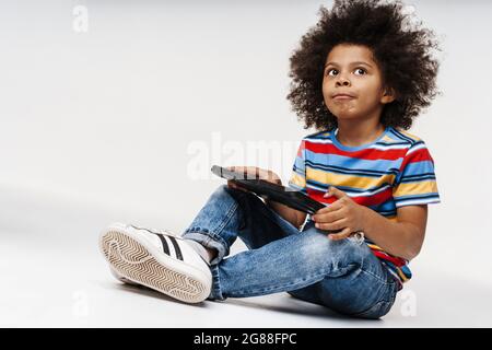 Close up of a little african kid holding tablet over red wall background, sitting on a floor Stock Photo