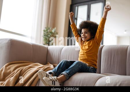 Black curly boy gesturing and using tablet computer while sitting on sofa at home Stock Photo