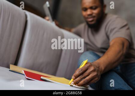 Black unshaven man using tablet computer while writing down notes at home Stock Photo