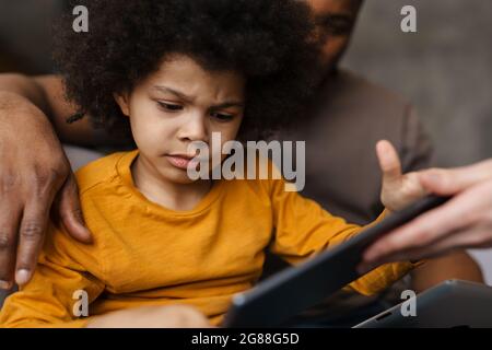 Black father and son using tablet computers while sitting on sofa at home Stock Photo