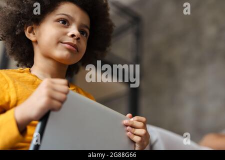 Black curly boy using tablet computer while sitting on sofa at home Stock Photo