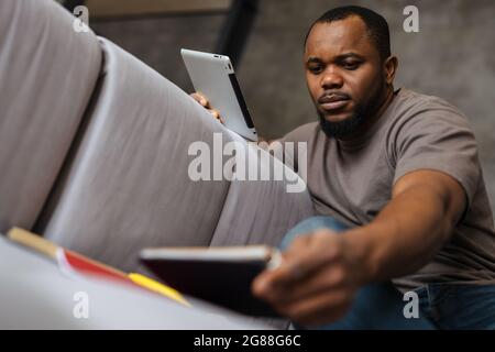 Black unshaven man using tablet computer while working at home Stock Photo