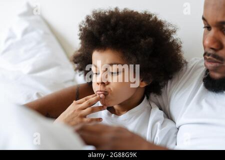 Black father and son using tablet computer while lying in bed at home Stock Photo