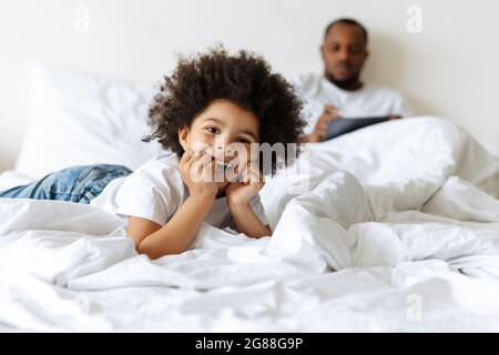 Black boy laughing while his father using tablet computer in bed at home Stock Photo