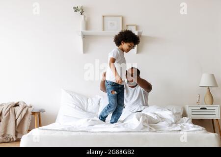 Black boy smiling while playing with her father on bed at home Stock Photo