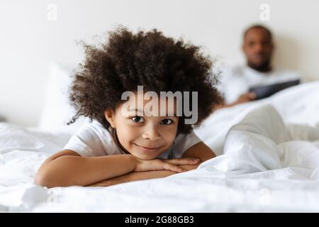 Black boy smiling while his father using tablet computer in bed at home Stock Photo