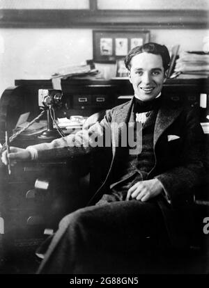 Portrait of silent film star Charlie Chaplin, around 1915–1920. Chaplin sitting at a desk smiling and looking relaxed. Stock Photo