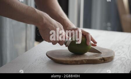 Man cutting ripe mango on olive board on white oak table, wide photo Stock Photo