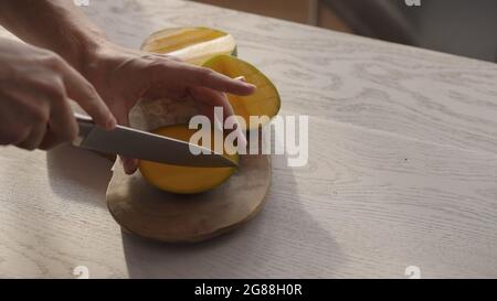 Man cutting ripe mango on olive board on white oak table, wide photo Stock Photo
