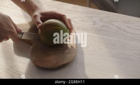 Man cutting ripe mango on olive board on white oak table, wide photo Stock Photo