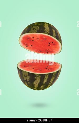 Ripe watermelon cut in half flying in the air. Floating, flying, levitating sliced fresh watermelon on a green background. Creative and abstract food Stock Photo