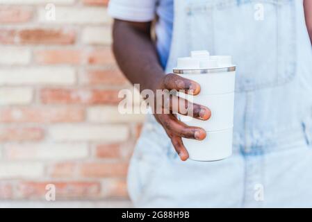 hands of an unrecognizable afro man holding a reusable cup of coffee. He has deteriorated skin Stock Photo
