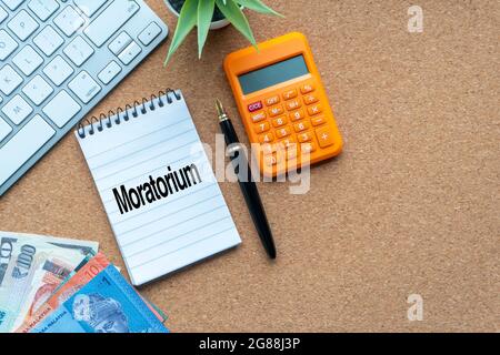 MORATORIUM text with notepad, calculator, decorative plant, money banknotes, keyboard and fountain pen on wooden background. Business and copy space c Stock Photo