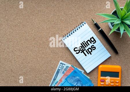 SELLING TIPS text with notepad, calculator, decorative plant, money banknotes, keyboard and fountain pen on wooden background. Business and copy space Stock Photo