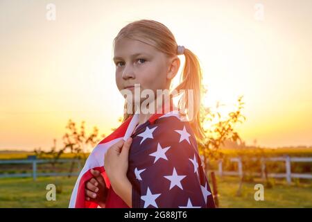 Portrait of a cute little girl, wrapped in an American flag, standing in a field Stock Photo