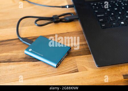 A blue Samsung 500GB encrypted solid state drive (SSD) external portable drive for data backup with a USB-C connection cable connecting it to a laptop Stock Photo