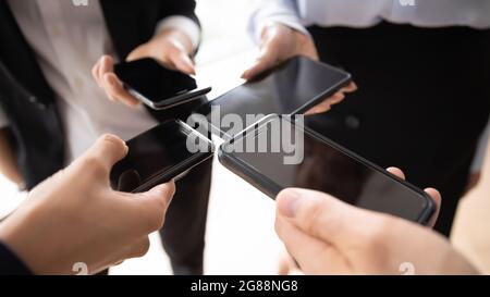 Business group standing in circle, holding similar mobile phones together Stock Photo