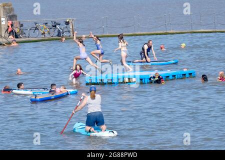 Clevedon, Somerset, UK. 18th July, 2021. Clevedon Marine Lake draws in people looking to cool down on a very hot day. Paddle boarding, jumping in and swimming are on the family fun agenda before freedom day tomorrow. Credit: JMF News/Alamy Live News Stock Photo