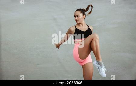 Woman in sportswear and doing warming up workout. Female athlete doing exercise routine against grey background. Stock Photo