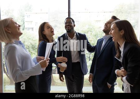 Happy relaxed diverse office colleagues having fun in hallway Stock Photo