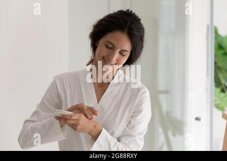 Happy millennial female apply cream for sensitive skin on hands Stock Photo