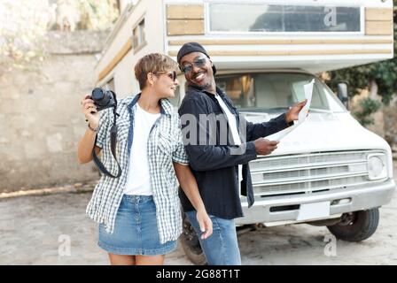 Summer travel concept - Multiracial middle age couple or friends looking at map to plan a camper van road trip.African and latin ethnic. Holding big T Stock Photo
