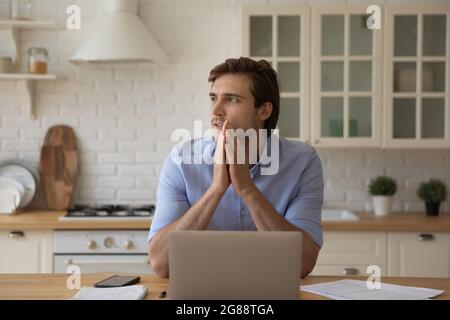 Young male studying at kitchen pondering distracted from laptop screen Stock Photo