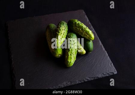 Natural fresh green cucumbers from a home garden on a black background, a dummy board made of stone. View from above. Stock Photo