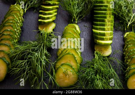 Natural fresh green cucumbers from a home garden on a black background, a dummy board made of stone. The cucumbers are cut into pieces and arranged in Stock Photo