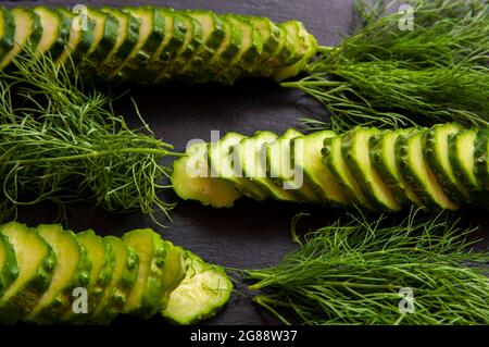 Natural fresh green cucumbers from a home garden on a black background, a dummy board made of stone. The cucumbers are cut into pieces and arranged in Stock Photo