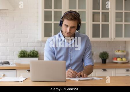 Young male in headset look on pc screen take notes Stock Photo