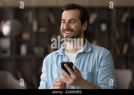 Happy dreamy young man holding smartphone in hands. Stock Photo