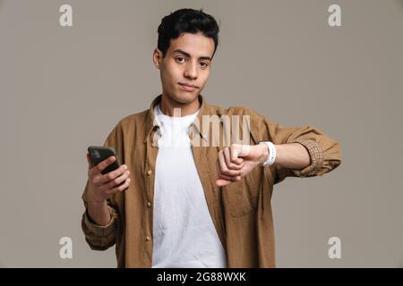 Brunette hispanic man using cellphone and smartwatch isolated over grey background Stock Photo