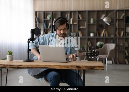 Focused young man in headphones playing guitar in home studio. Stock Photo