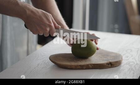 Man cutting ripe mango on olive board on white oak table, wide photo Stock Photo