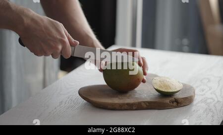 Man cutting ripe mango on olive board on white oak table, wide photo Stock Photo