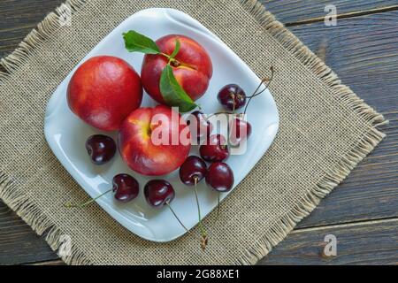 Fresh ripe cherries and nectarines on white plate. Rustic table. Flat lay Stock Photo