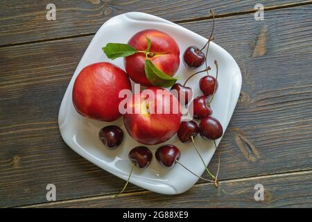 Fresh ripe fruits - cherries and nectarines - on white plate. Rustic background. Flat lay, copy space Stock Photo