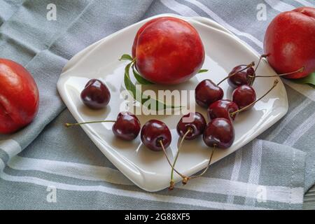 Red fruits. Fresh ripe cherries and nectarines on white plate Stock Photo