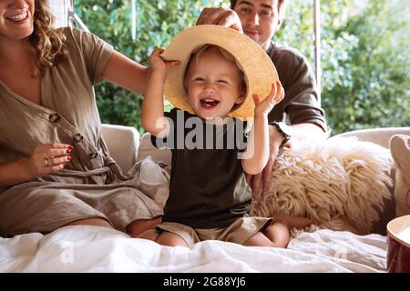 Portrait of cute small boy in straw hat with parents in cozy bedroom rv with window in summer forest
