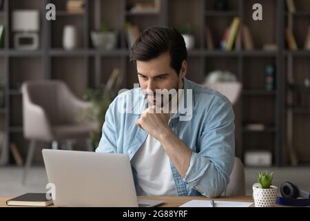 Concentrated millennial man working on computer at home office. Stock Photo