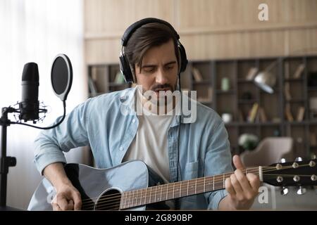 Happy millennial male musician playing guitar, recording own music. Stock Photo