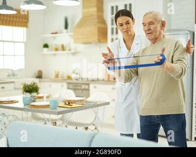 Aged man holding a fitness rubber band in his apartment Stock Photo