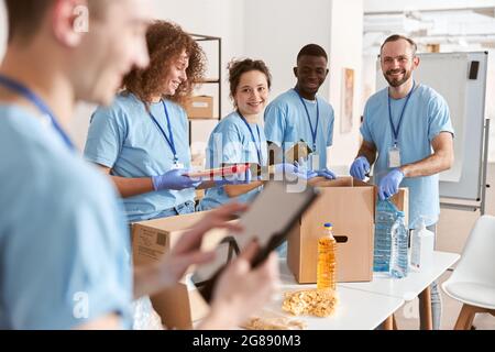 Smiling diverse volunteers sorting foodstuff in cardboard boxes, working together on donation project Stock Photo