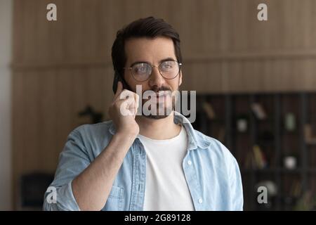 Happy young man in eyeglasses holding cellphone conversation. Stock Photo