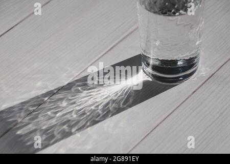Glass of water on white table in sunlight casting shadow Stock Photo