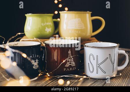 Lviv, Ukraine - December 1, 2017: Many cute cups on wooden table on black background with christmas lights. Different mugs for family. Stylish gift fo Stock Photo