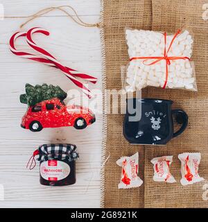 Lviv, Ukraine - December 1, 2017: Homemade jam, marshmallow, cup, raffaello, candy cane, car with tree on burlap and white table top view. Stylish swe Stock Photo