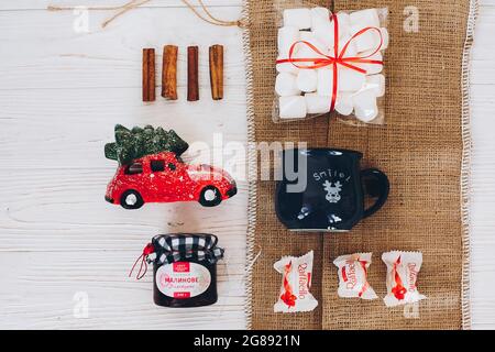 Lviv, Ukraine - December 1, 2017: Homemade jam, marshmallow, cup, raffaello, cinnamon, car with tree on burlap and white table top view. Stylish sweet Stock Photo